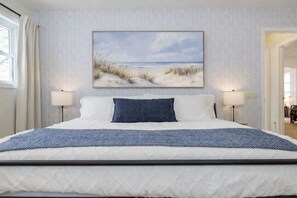 Een slaapkamer met een bed, twee bedlampen, een wanddecoratie van een strandschilderij en een behang met een patroon.