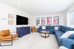 Een moderne woonkamer met een blauwe bank, een bruine leren fauteuil, een blauwe kast, een ronde salontafel en een flatscreen televisie aan de muur.