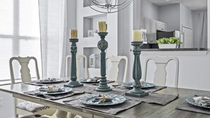 A dining table with three candle holders, a white cabinet, and a kitchen area in the background.