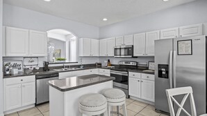 A modern kitchen with white cabinetry, a central island with stools, stainless steel appliances, and a welcome sign on the refrigerator.
