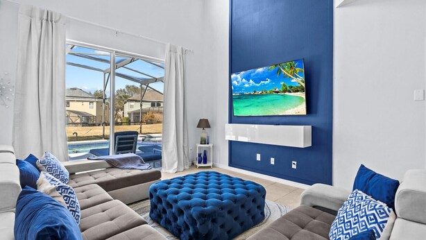 A modern living room with a pool view, a large flat-screen TV, and a blue accent wall.