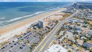 An aerial view of a coastal city with a beach, a hotel with a crane, and a road leading to the beach. - Beachfront Bliss in the Heart of Daytona! Directly on the beach. Heated pool. (Daytona beach)