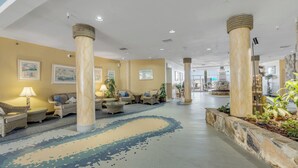 A spacious lobby with high ceilings, large columns, and a patterned floor. Furnishings include sofas and chairs arranged around a central area with potted plants. - Beachfront Bliss in the Heart of Daytona! Directly on the beach. Heated pool. (Daytona beach)