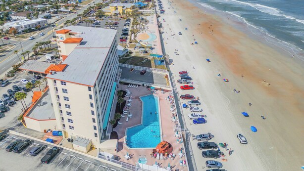 An aerial view of a coastal hotel with a swimming pool, beach access, and a parking area. - Beachfront Bliss in the Heart of Daytona! Directly on the beach. Heated pool. (Daytona beach)