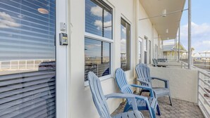 A covered outdoor area with two blue chairs, a white railing, and a view of the beach through the windows. - Beachfront Bliss in the Heart of Daytona! Directly on the beach. Heated pool. (Daytona beach)