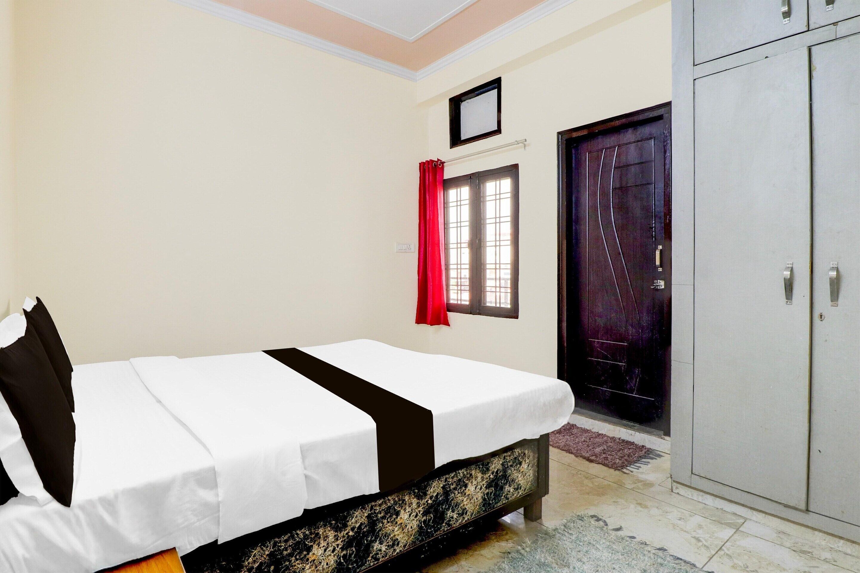 Un dormitorio con cama, armario, puerta y ventana con cortinas rojas.