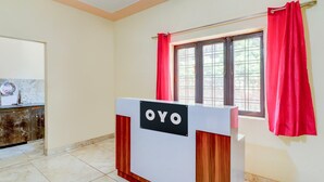 En receptionsdisk med et skilt, der siger "OYO", i et rum med flisegulv og et vindue med røde gardiner.