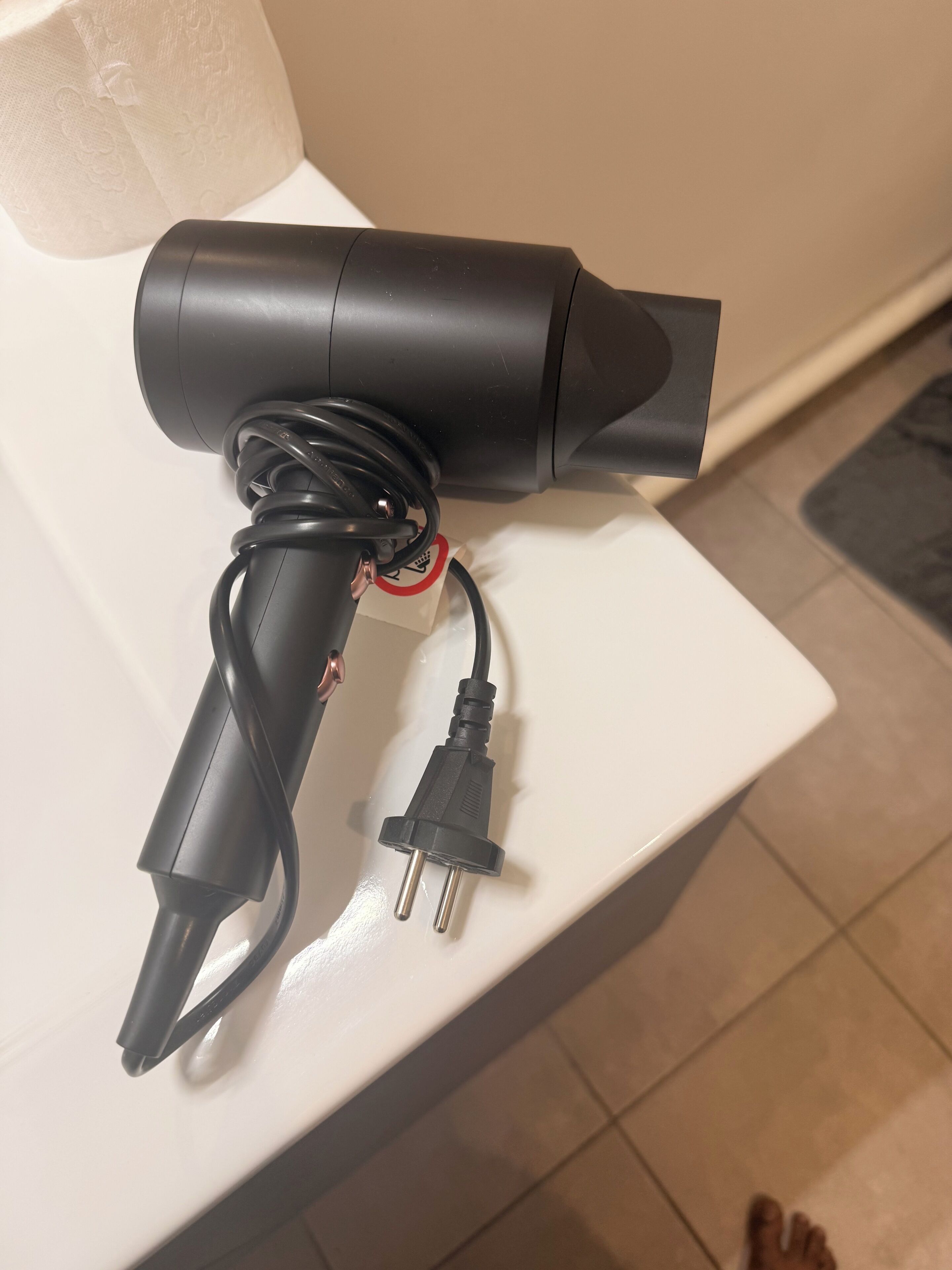 Un secador de pelo sobre una superficie blanca, con cable y enchufe.