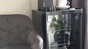 Un refrigerador petit amb una ampolla d'aigua a dins, una tassa blanca a la part superior i una petita planta a la porta.