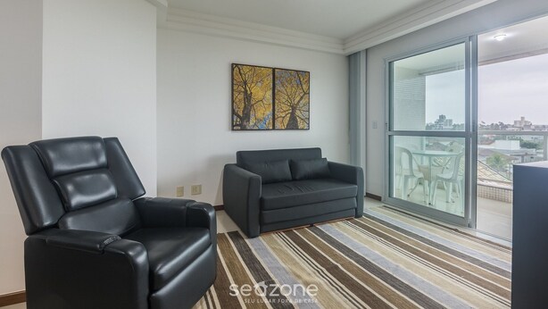Un salon moderne avec un canapé en cuir noir, un fauteuil noir et un canapé gris. Une grande fenêtre offre une vue sur la ville.