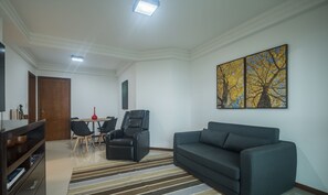 Una sala de estar con un sofá, un televisor, una mesa de comedor con sillas y un cuadro en la pared.