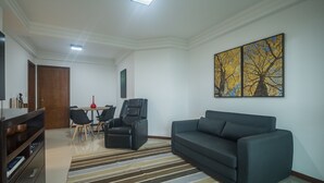 Un salon comprenant un canapé, un téléviseur, une table à manger avec des chaises et un tableau accroché au mur.