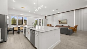A modern kitchen with a large island, a dining area with chairs, and a living room with a sofa and a TV. - Last Minute Disney Getaway! Luxury Villa with Private Pool, Hot Tub & Themed Bedrooms. Book Now! #147189 (Orlando)