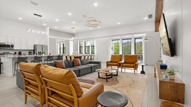 A modern living room with a sofa, chairs, and a coffee table. There is a kitchen area with cabinets and appliances. - Last Minute Disney Getaway! Luxury Villa with Private Pool, Hot Tub & Themed Bedrooms. Book Now! #147189 (Orlando)