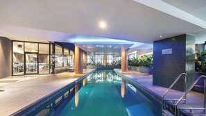 An indoor swimming pool with a wooden deck, glass walls, and a sign indicating a pool depth of 12 meters. - Southbank 2BDR With Views Gym Pool And Sauna (Southbank)