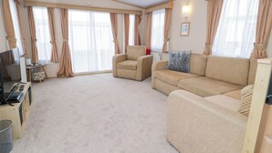 A spacious living room with a beige sofa, a small armchair, and a television on a wooden stand. - 11, Beachfields (Rhyl)