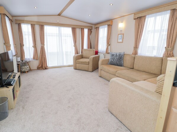 A spacious living room with a beige sofa, a small armchair, and a television on a wooden stand. - 11, Beachfields (Rhyl)