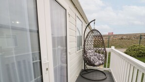 A balcony with a hanging chair, a white railing, and a view of a fenced area. - 11, Beachfields (Rhyl)