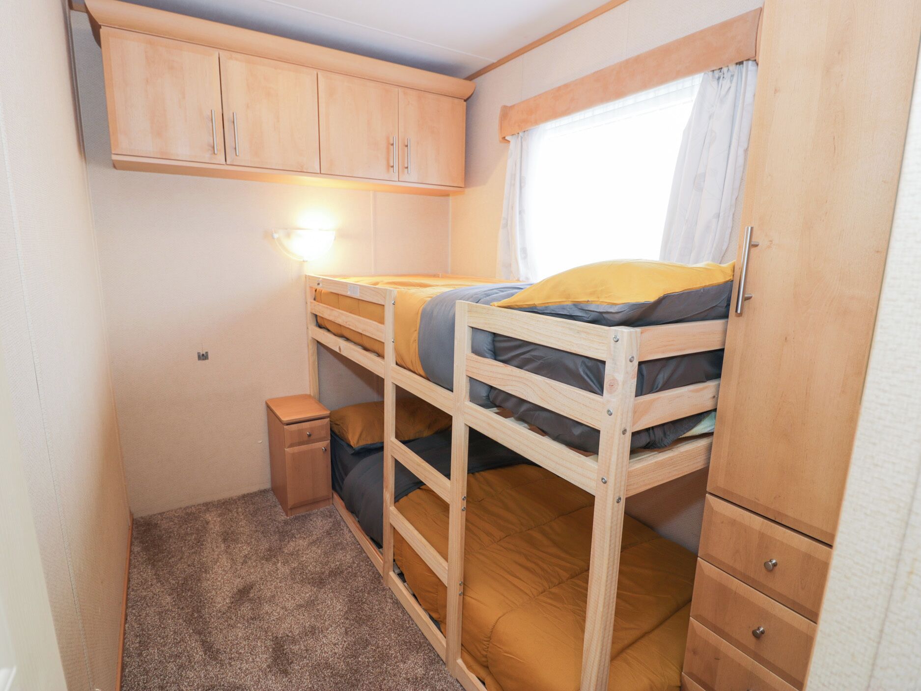 Une chambre à coucher de taille réduite, avec des lits superposés, une petite table de chevet et une armoire.