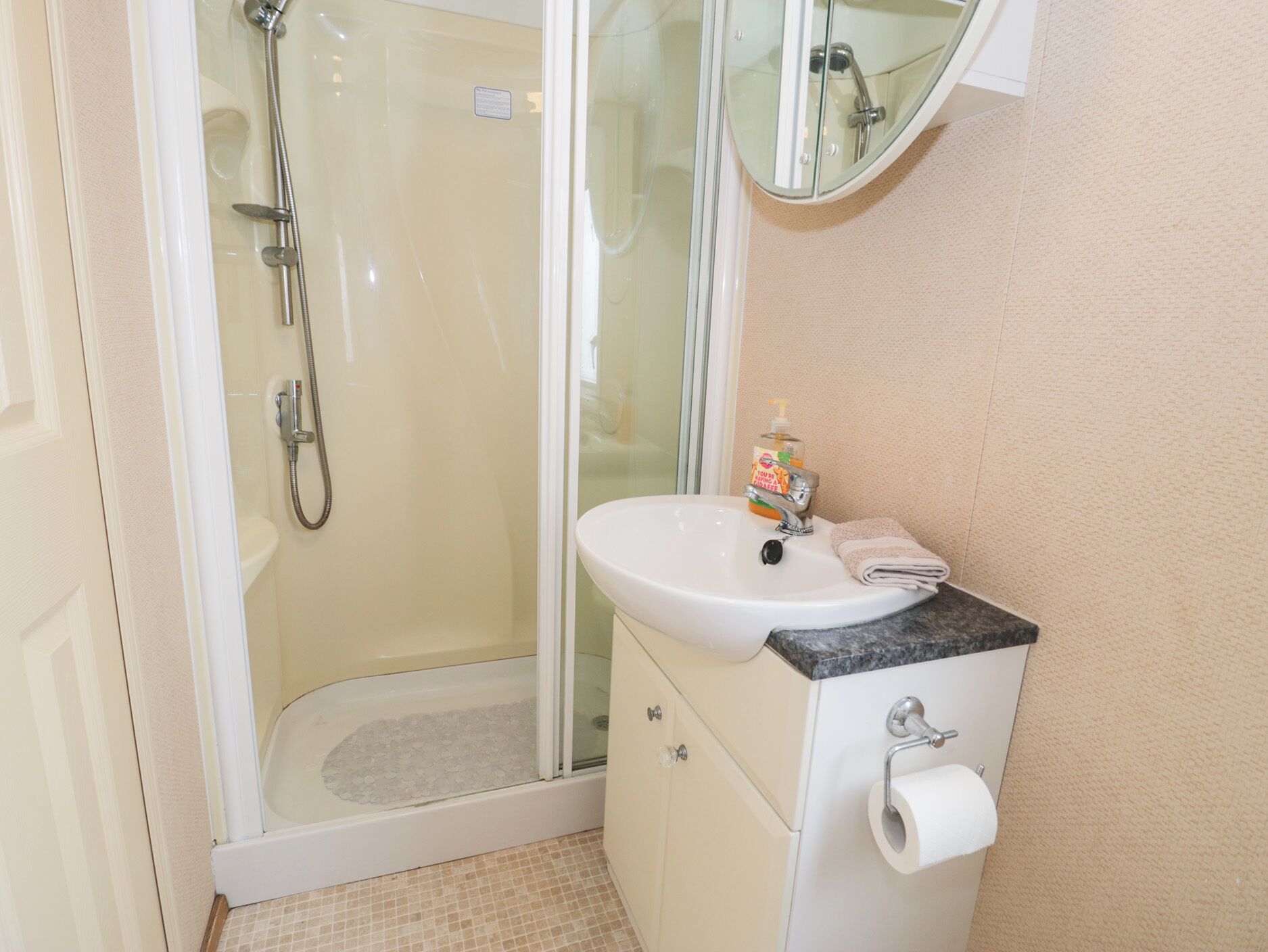 Un bagno con doccia vetrata, un lavandino bianco con piano in marmo e uno specchio sopra il lavandino.