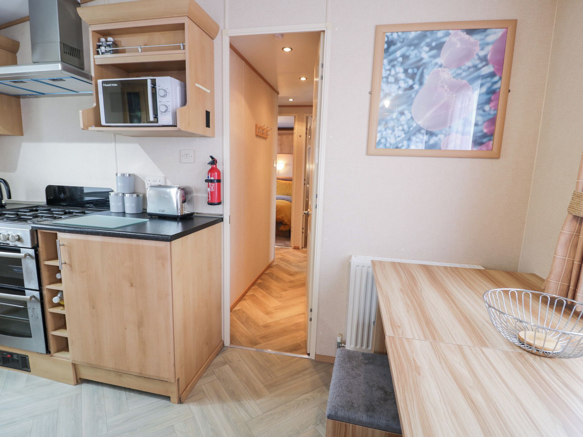 A compact kitchen with a microwave, toaster, and stove. There's a fire extinguisher on the wall and a framed picture above the counter.