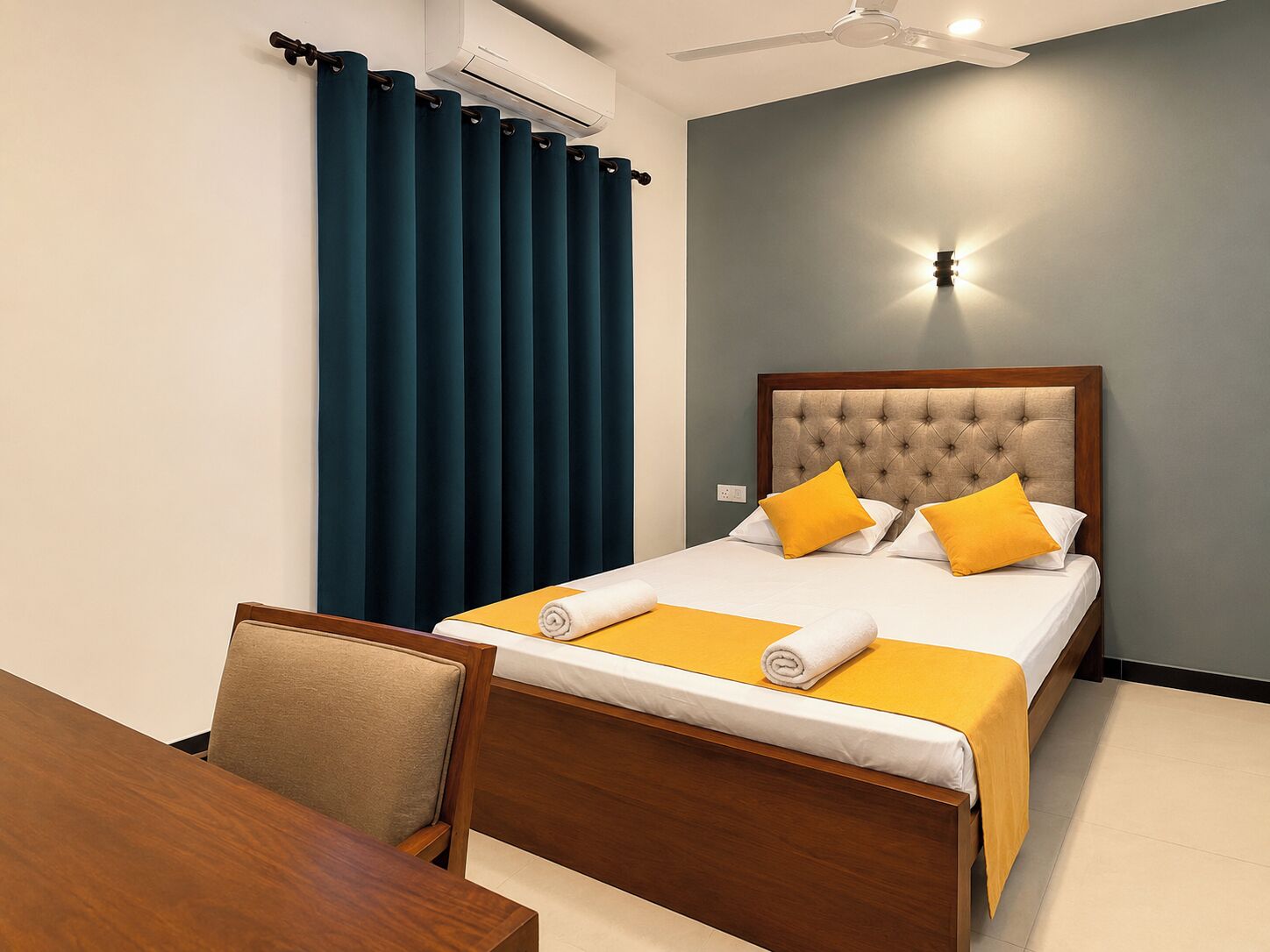 Una camera d'albergo con un letto, una scrivania, una sedia, un ventilatore a soffitto e un condizionatore d'aria a parete.