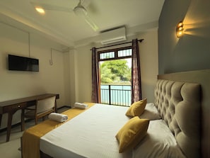 Habitación de hotel con cama, escritorio, televisor y balcón con vista a la vegetación.