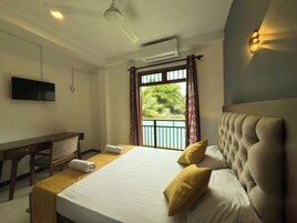 A hotel room with a bed, a desk, a television, and a balcony with a view of greenery.