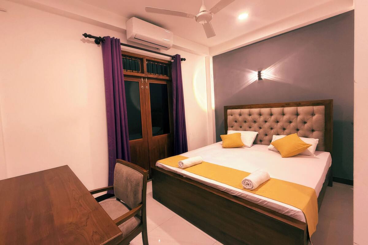 Habitación de hotel con cama, escritorio, silla, aire acondicionado y ventilador de techo.