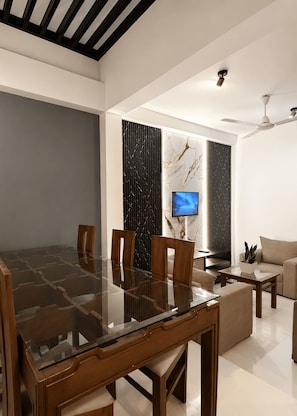 Una sala de estar moderna con una mesa de comedor de vidrio, sillas de madera, un sofá, un televisor y un ventilador de techo.