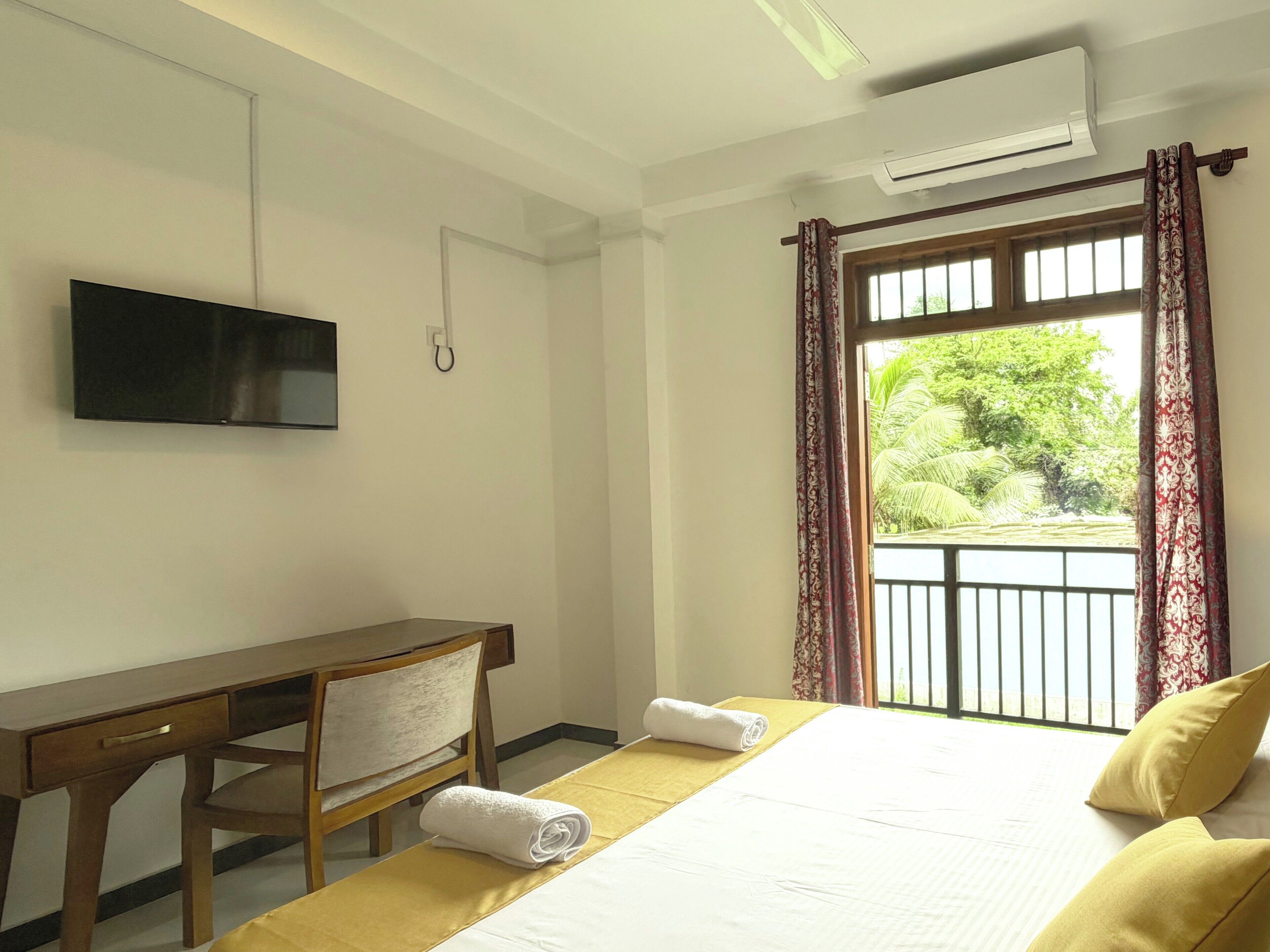 Una habitación de hotel con cama, escritorio, silla, televisión y ventana con cortinas.