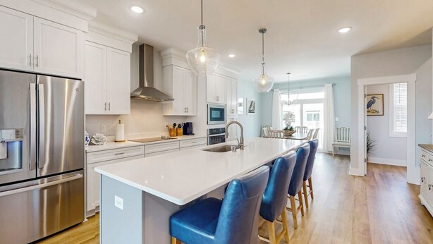 A modern kitchen with white cabinets, stainless steel appliances, a central island with bar stools, pendant lighting, and a view into the dining area.