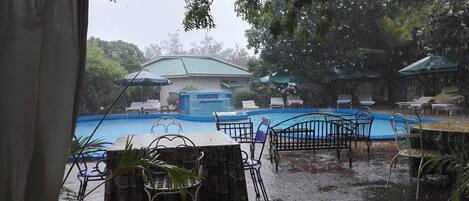 Vista de uma área de piscina com um espaço coberto para sentar e guarda-sóis.