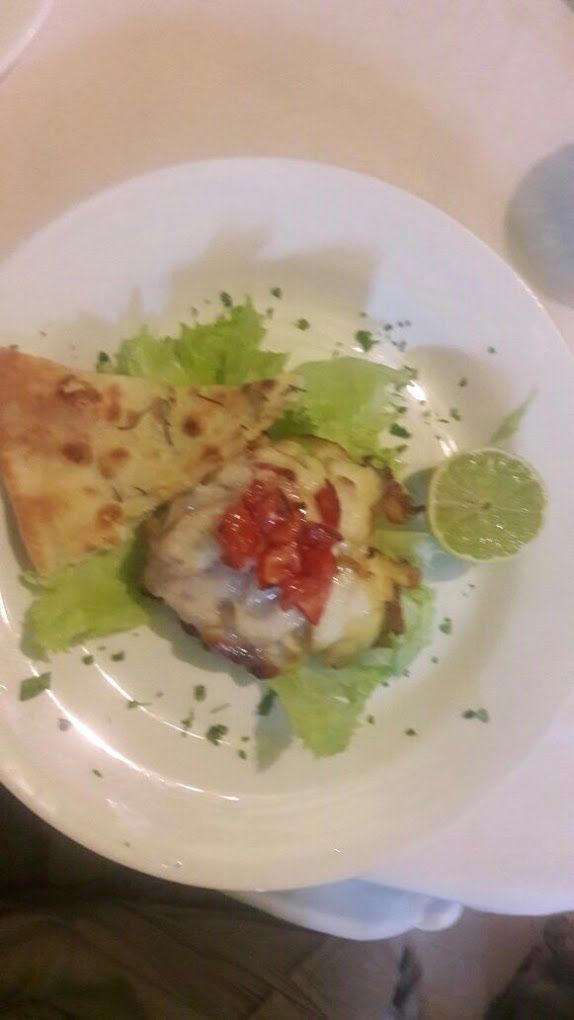 A plate with a grilled chicken breast, a slice of pizza, and a lime wedge.