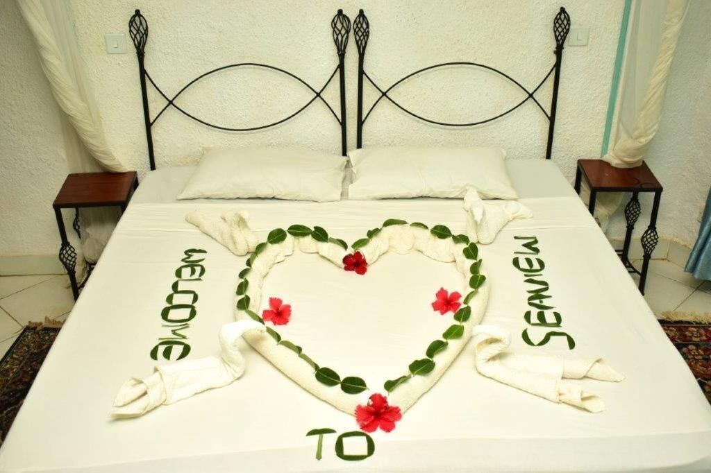 A bed with a heart-shaped floral arrangement in the center, flanked by towels with "WELCOME TO" and "SEANIEL" written on them.