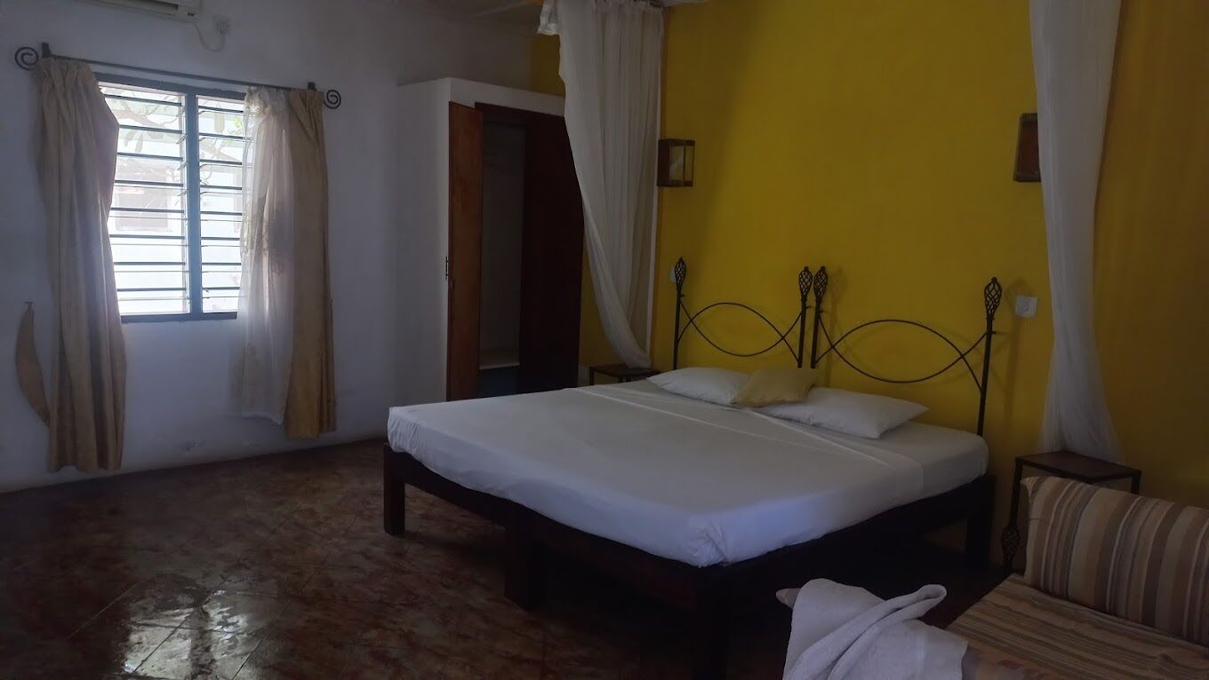 A bedroom with a bed, a window with curtains, a door, and a yellow wall.