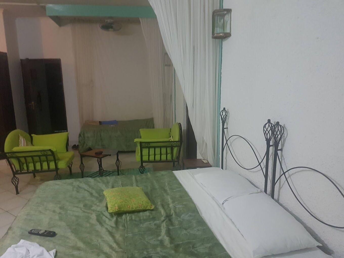 A room with a bed, two green chairs, a small table, and a TV.