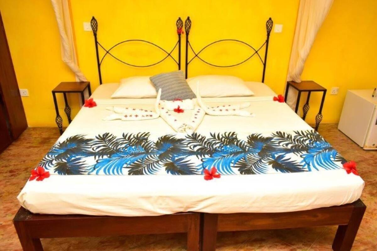 A bed with a tropical leaf bedspread, a metal headboard, and two bedside tables.