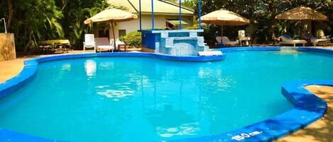 A swimming pool with a blue border, lounge chairs, umbrellas, and a gazebo structure.