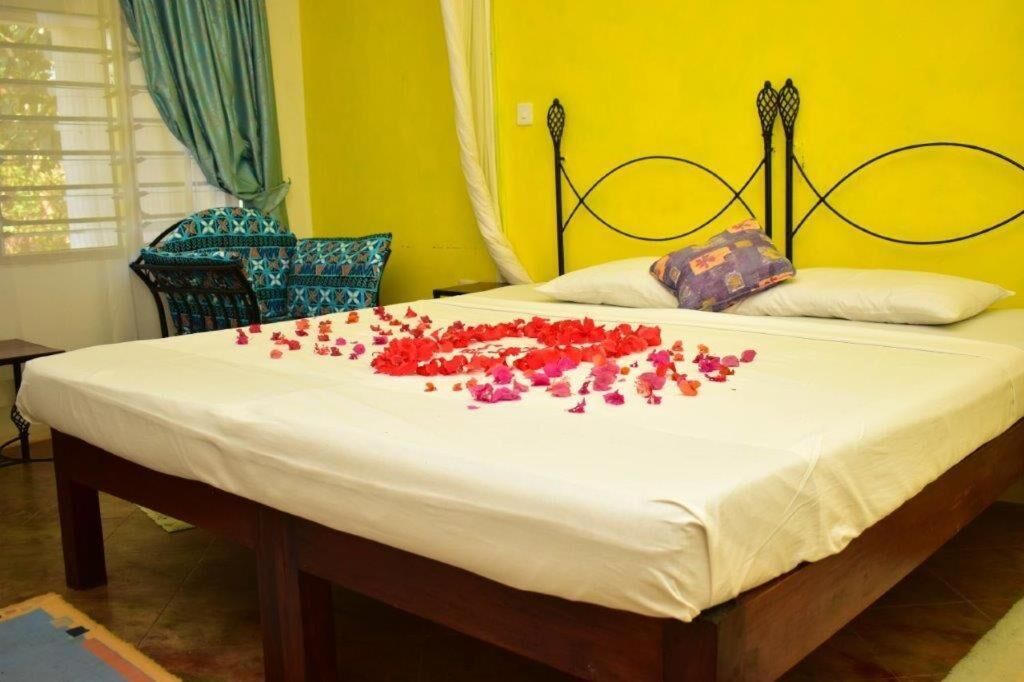 A bed with a white sheet and a floral arrangement of red and pink petals.