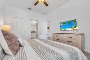 Une chambre à coucher comprenant un lit, une commode en bois, un téléviseur et une porte donnant sur une autre pièce.
