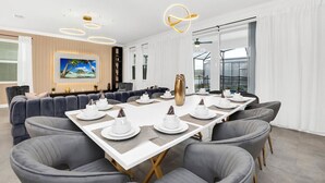 A modern dining area with a long table set for a meal, surrounded by grey upholstered chairs. - Last Minute Disney! Private Pool, Hot Tub, Game Room & Themed Bedrooms. Book Now! #118573 (Orlando)