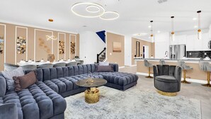A modern living room with a sectional sofa, a round coffee table, and a dining area with a kitchen in the background. - Last Minute Disney! Private Pool, Hot Tub, Game Room & Themed Bedrooms. Book Now! #118573 (Orlando)