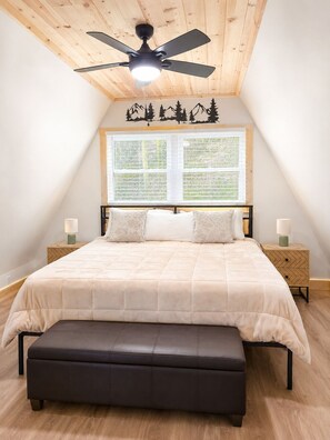 A bedroom with a bed, a ceiling fan, a window with blinds, and a nightstand with a lamp. - Cozy Cabin Retreat - Relax & Unwind in Wytheville (Wytheville)