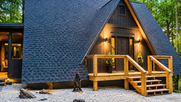 Uma cabana moderna com telhado íngreme, deck de madeira e entrada com piso de pedra.