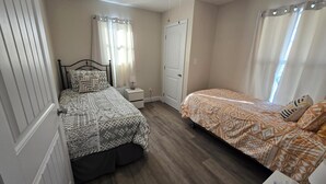 A bedroom with two beds, a nightstand, a door, and a window with curtains. - Shawnee Forest Retreat, Suite A, near Garden of the Gods, Southern IL (Harrisburg)