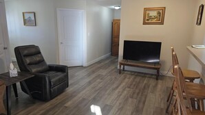 A living room with a black leather chair, a wooden bench, a flat-screen TV, and a wooden cabinet. - Shawnee Forest Retreat, Suite A, near Garden of the Gods, Southern IL (Harrisburg)