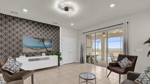 Un salon moderne avec une console blanche, deux fauteuils marron, une table basse en verre et un grand tableau sur le thème de la plage accroché au mur.