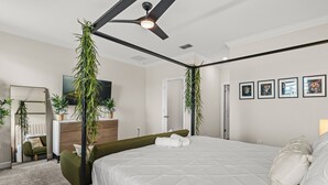 Une chambre moderne avec un lit à baldaquin, un ventilateur de plafond et plusieurs plantes en pot.