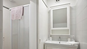 Un bagno moderno con box doccia in vetro, un mobile vanitario bianco con specchio e un portascopevoli.